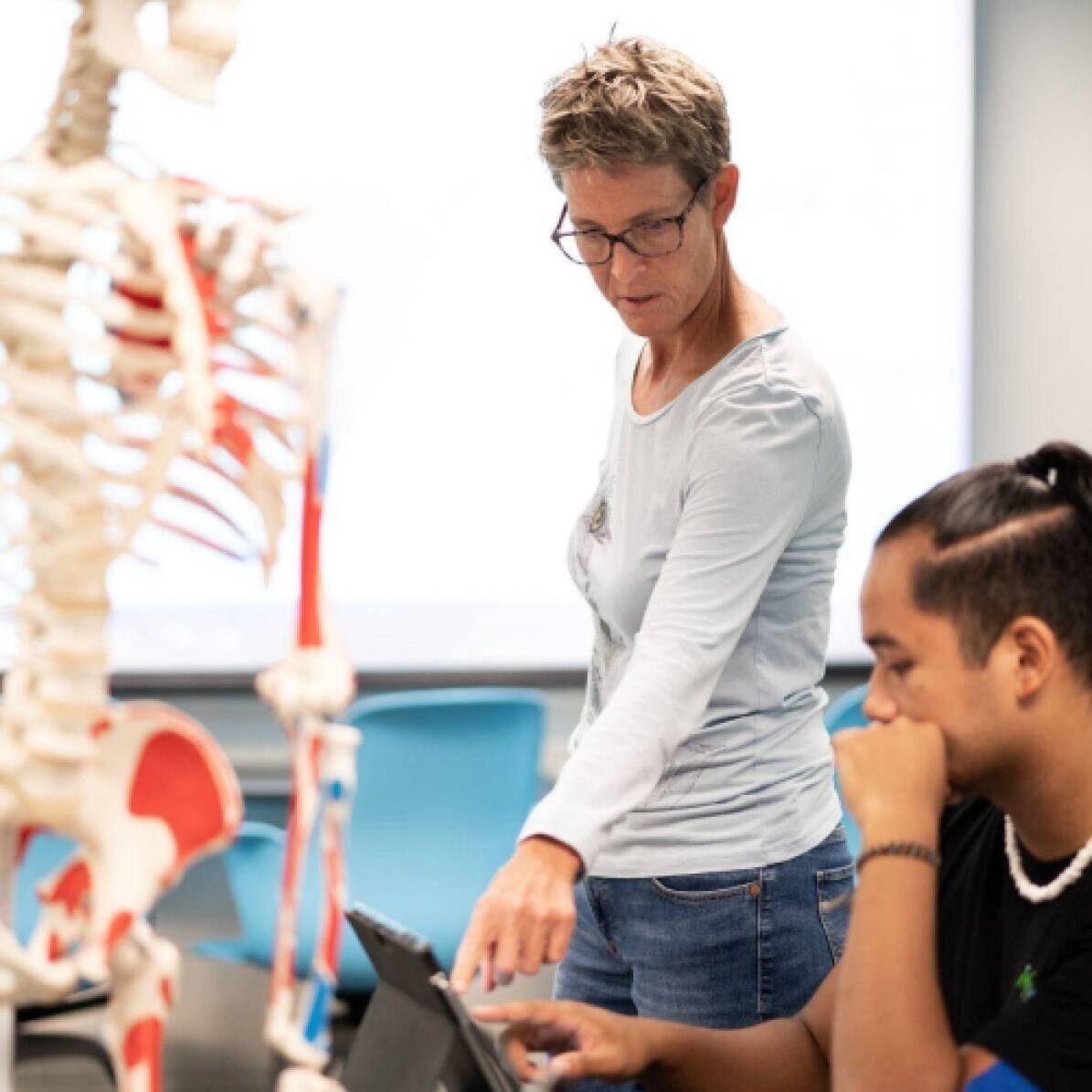A professor standing next to a student explaining something while pointing to the student's paper